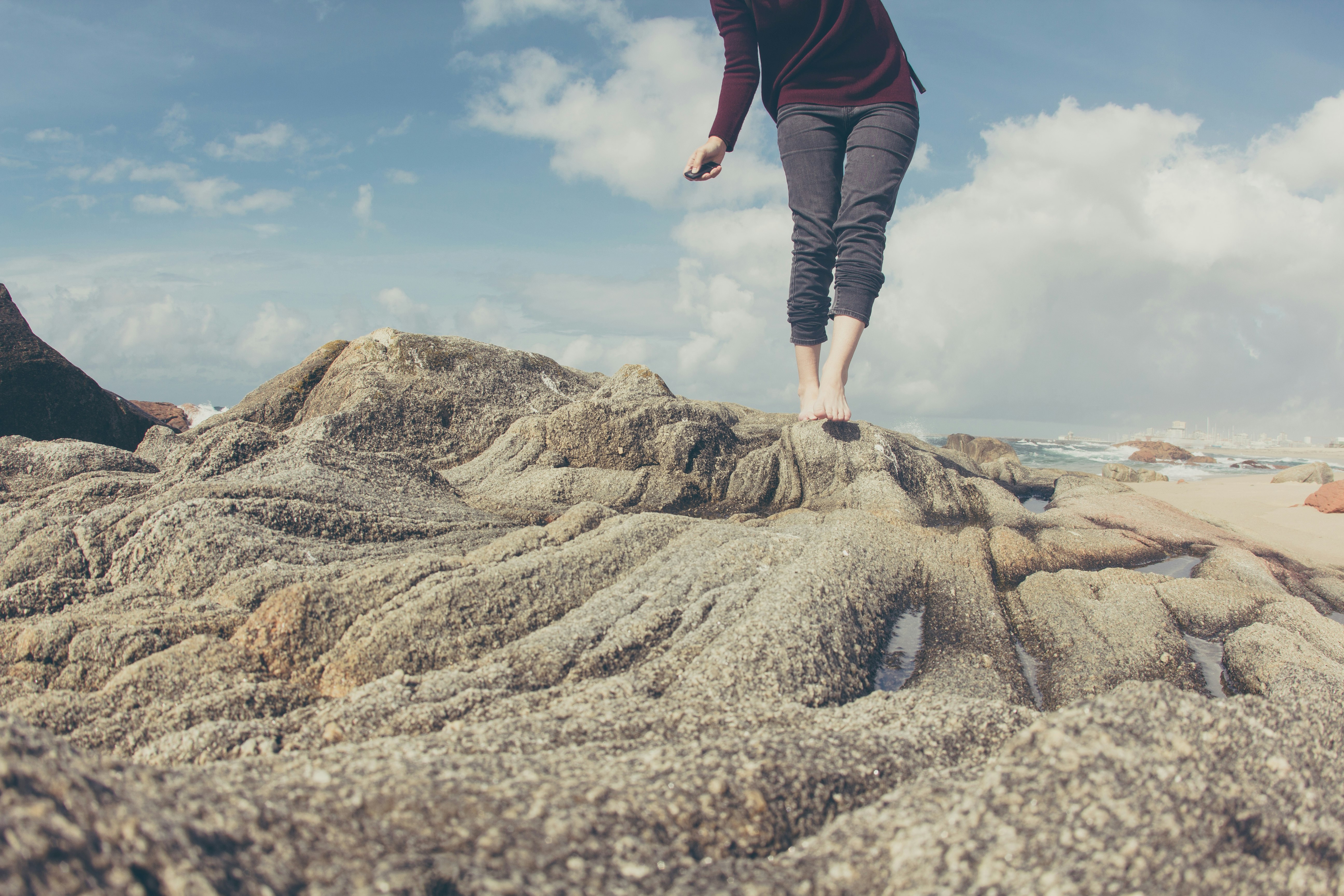 person wearing gray pants standing on gray rock formation under blue and white sky during daytime